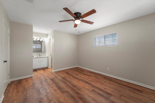 unfurnished bedroom featuring ceiling fan, sink, ensuite bathroom, wood-type flooring, and a textured ceiling