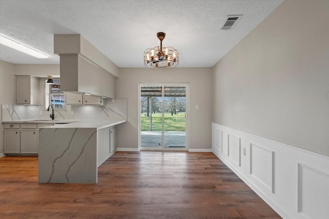 kitchen with sink, dark wood-type flooring, a notable chandelier, kitchen peninsula, and pendant lighting