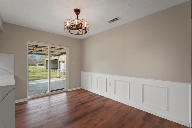 empty room featuring a chandelier, a textured ceiling, and hardwood / wood-style flooring