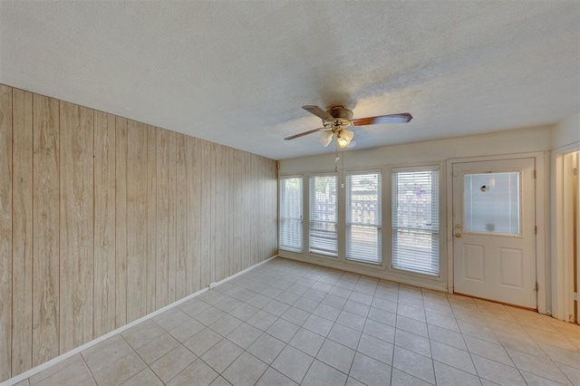 empty room featuring light tile patterned floors, ceiling fan, and wood walls