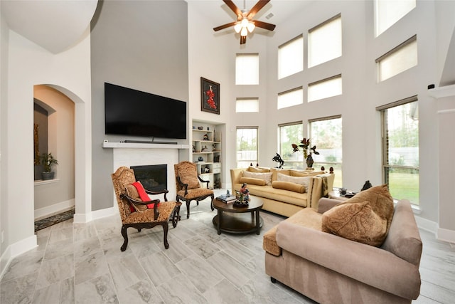 living room featuring built in shelves, ceiling fan, and a high ceiling