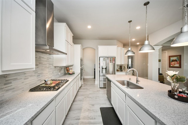 kitchen featuring sink, white cabinetry, pendant lighting, light stone countertops, and wall chimney range hood