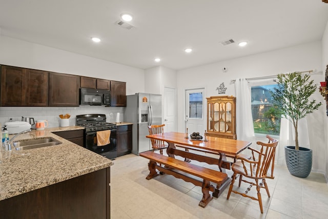 kitchen featuring sink, light stone counters, decorative backsplash, dark brown cabinets, and black appliances