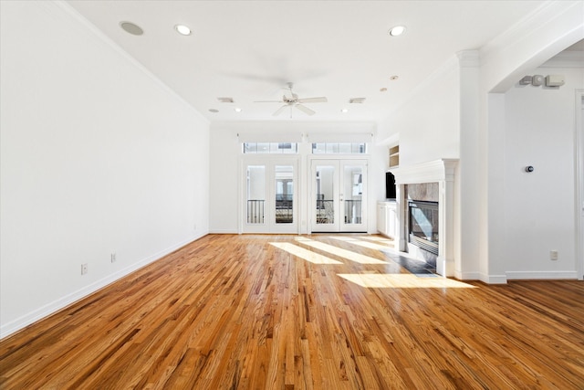 unfurnished living room featuring ceiling fan, a tile fireplace, crown molding, and light wood-type flooring