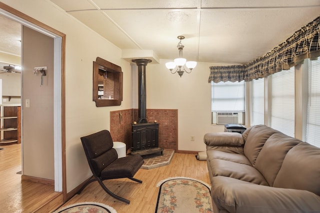 living room featuring a wood stove, cooling unit, wood-type flooring, and ceiling fan with notable chandelier