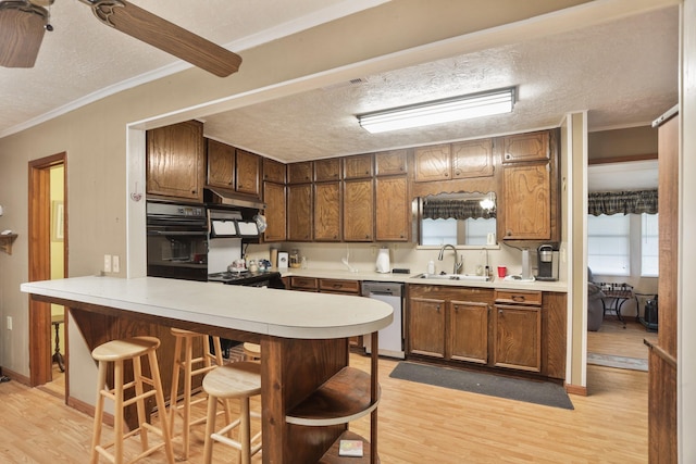 kitchen with a textured ceiling, sink, dishwasher, black oven, and a breakfast bar area