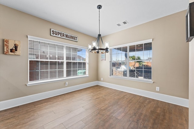 empty room featuring wood-type flooring and a notable chandelier