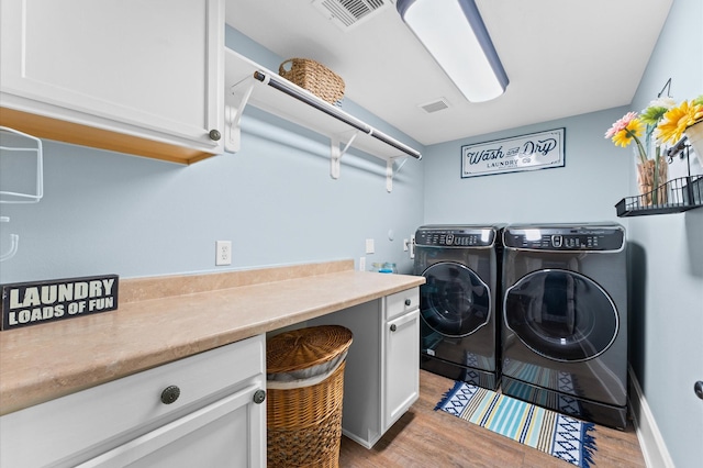 laundry room with cabinets, washer and dryer, and light hardwood / wood-style floors