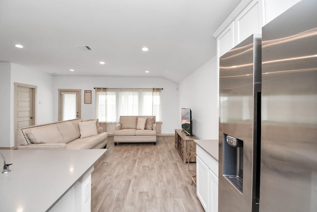 kitchen with lofted ceiling, stainless steel fridge, light wood-type flooring, and white cabinetry