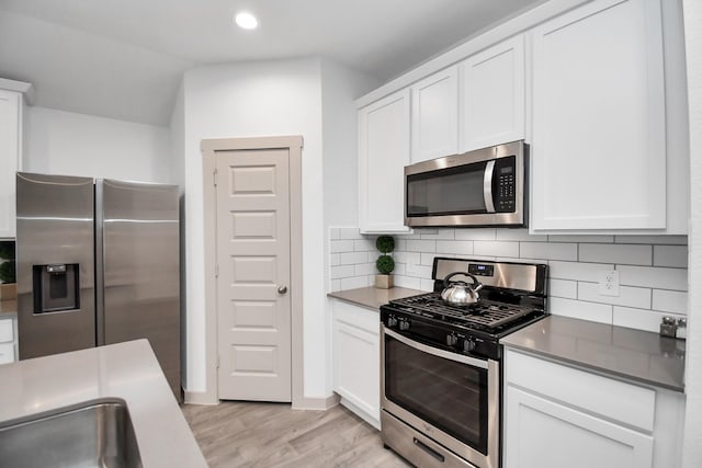 kitchen with light hardwood / wood-style floors, white cabinetry, backsplash, and appliances with stainless steel finishes