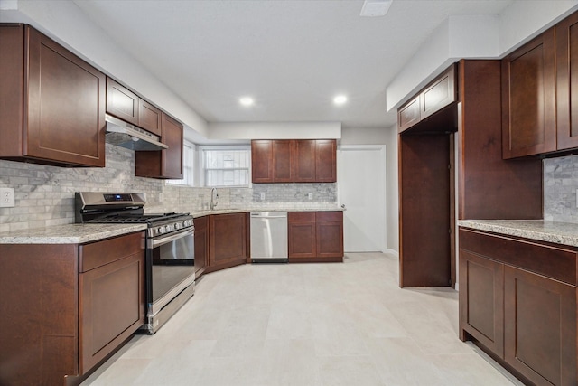 kitchen with backsplash, light stone counters, dark brown cabinets, stainless steel appliances, and sink