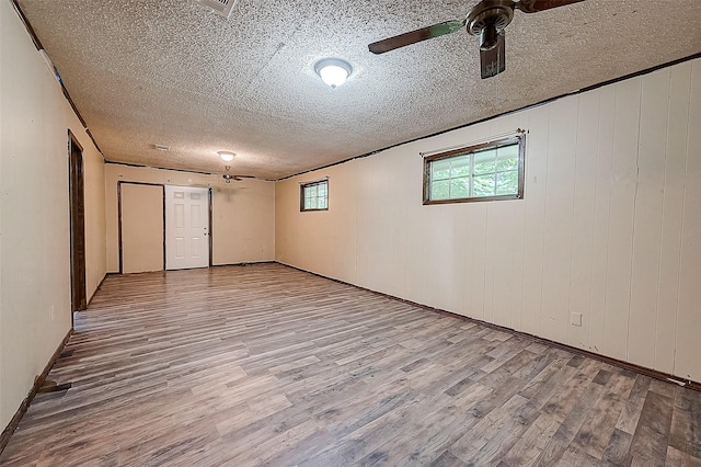 basement featuring ceiling fan, wood walls, and light hardwood / wood-style flooring