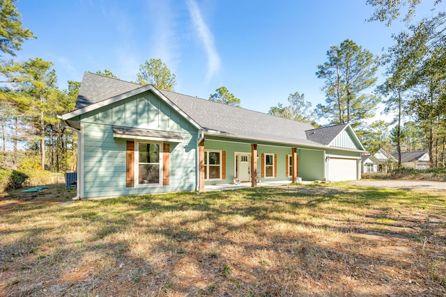 view of front of house featuring board and batten siding, a front yard, covered porch, driveway, and an attached garage