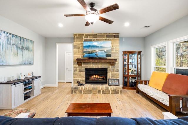 living room featuring hardwood / wood-style floors, baseboards, visible vents, ceiling fan, and a stone fireplace