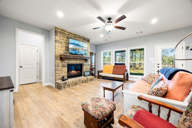 living area with visible vents, a stone fireplace, wood finished floors, and a ceiling fan