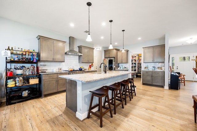 kitchen with wall chimney range hood, light stone counters, light wood-style flooring, stainless steel appliances, and a sink