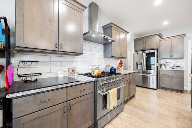 kitchen featuring recessed lighting, light wood-style floors, appliances with stainless steel finishes, wall chimney exhaust hood, and tasteful backsplash