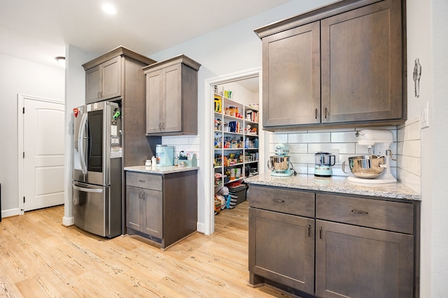 kitchen featuring light stone counters, tasteful backsplash, light wood-style flooring, and stainless steel fridge with ice dispenser