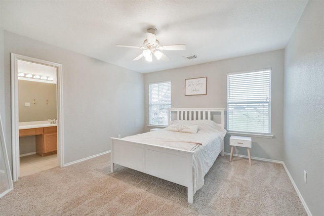 bedroom with ceiling fan, light colored carpet, and connected bathroom