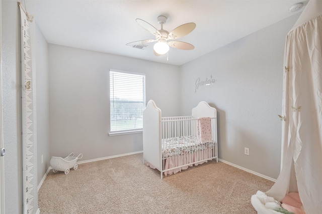 bedroom with ceiling fan, light colored carpet, and a crib