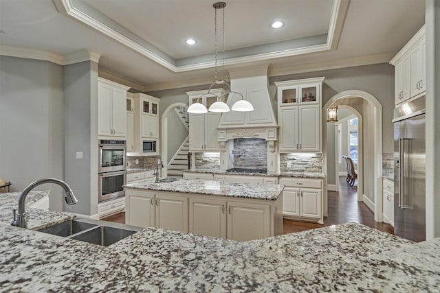 kitchen with sink, a raised ceiling, light stone counters, pendant lighting, and a kitchen island