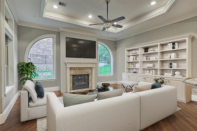 living room featuring a tile fireplace, a raised ceiling, crown molding, dark hardwood / wood-style floors, and ceiling fan