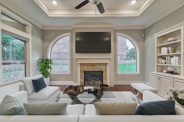 living room featuring ornamental molding, a tray ceiling, ceiling fan, a fireplace, and hardwood / wood-style floors