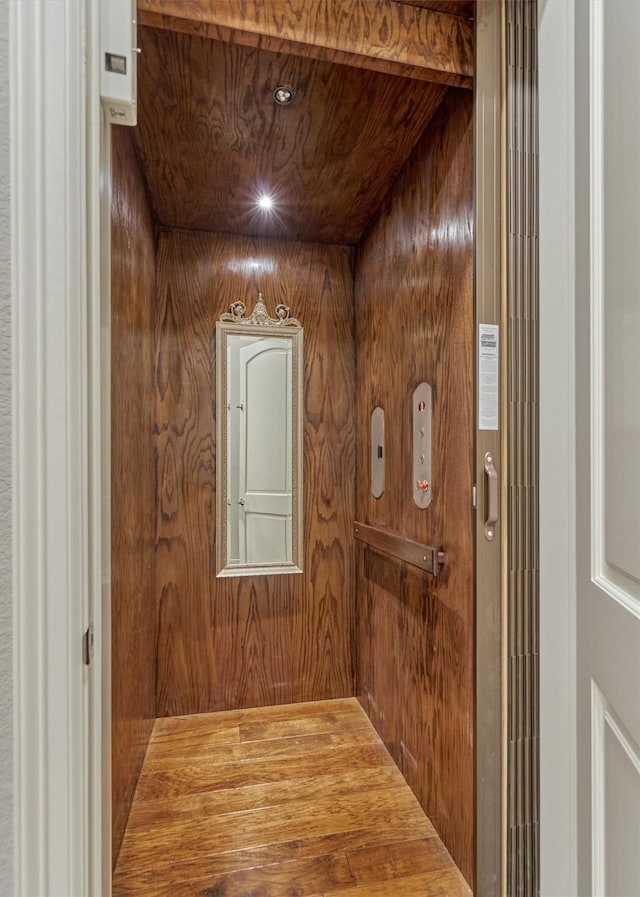 hallway featuring elevator, wooden walls, and wood ceiling