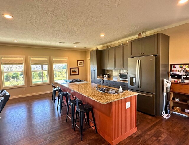 kitchen with a center island with sink, sink, stainless steel refrigerator with ice dispenser, light stone counters, and a breakfast bar area