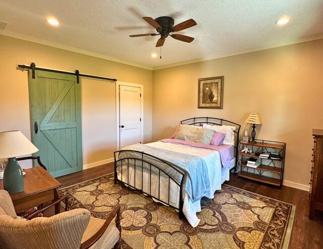 bedroom with a textured ceiling, ceiling fan, a barn door, and dark wood-type flooring