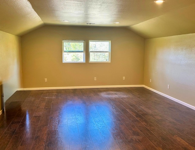 additional living space with a textured ceiling, dark wood-type flooring, and lofted ceiling