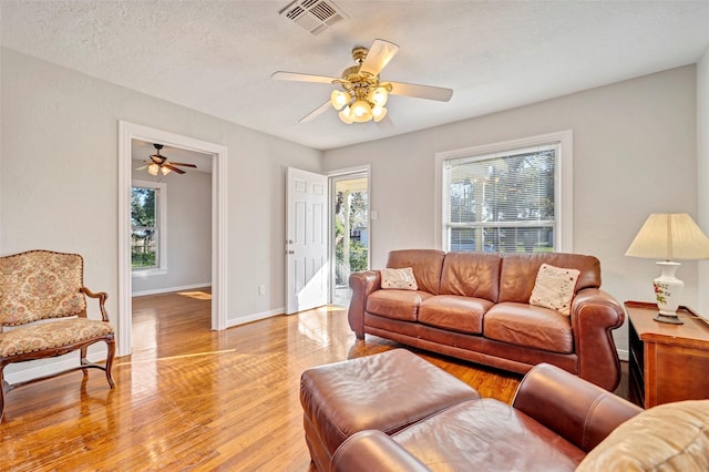 living room featuring a textured ceiling, light hardwood / wood-style floors, ceiling fan, and a healthy amount of sunlight