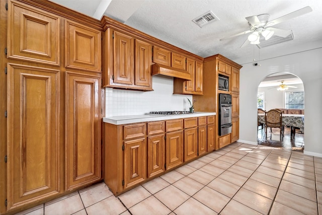 kitchen featuring ceiling fan, a textured ceiling, tasteful backsplash, wall oven, and light tile patterned flooring