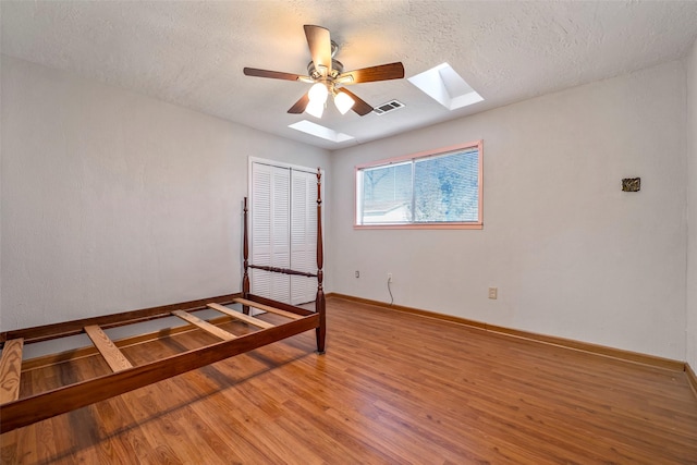 unfurnished bedroom with a skylight, ceiling fan, a textured ceiling, wood-type flooring, and a closet