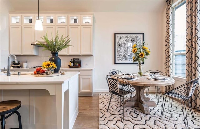 kitchen featuring backsplash, sink, light wood-type flooring, and hanging light fixtures