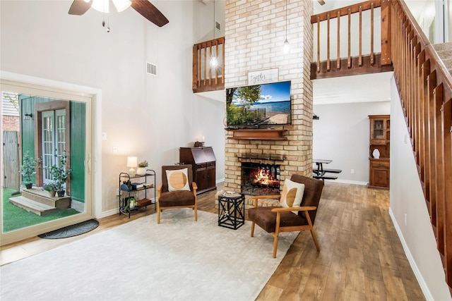 sitting room with a fireplace, a towering ceiling, hardwood / wood-style flooring, and ceiling fan