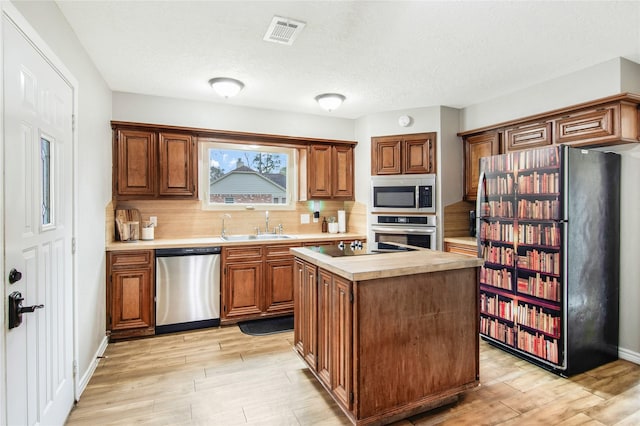 kitchen with light wood-type flooring, tasteful backsplash, stainless steel appliances, sink, and a center island