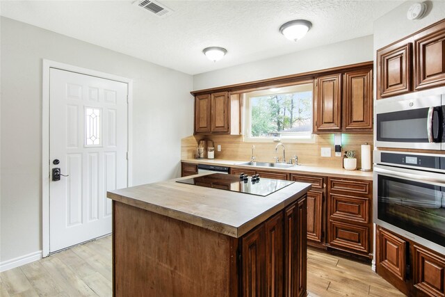 kitchen featuring decorative backsplash, stainless steel appliances, sink, light hardwood / wood-style flooring, and a center island