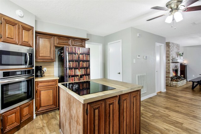 kitchen featuring light wood-type flooring, a brick fireplace, a textured ceiling, stainless steel appliances, and a kitchen island