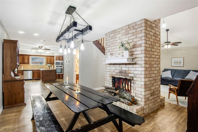 dining space with light wood-type flooring, a brick fireplace, and ceiling fan