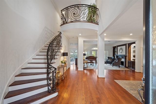 entrance foyer with crown molding, a towering ceiling, hardwood / wood-style floors, and decorative columns