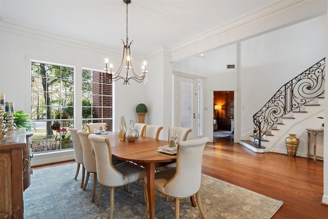 dining area with wood-type flooring, ornamental molding, and an inviting chandelier