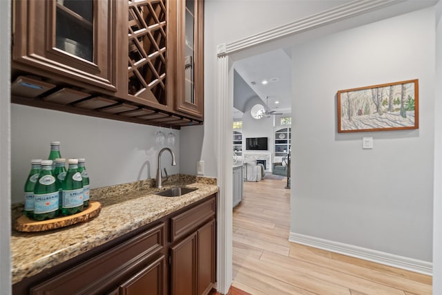 bar with light stone countertops, sink, and light wood-type flooring