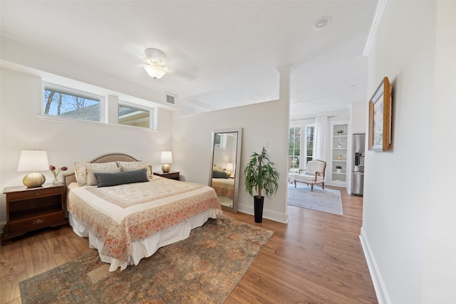 bedroom featuring wood-type flooring, ornamental molding, and stainless steel fridge with ice dispenser