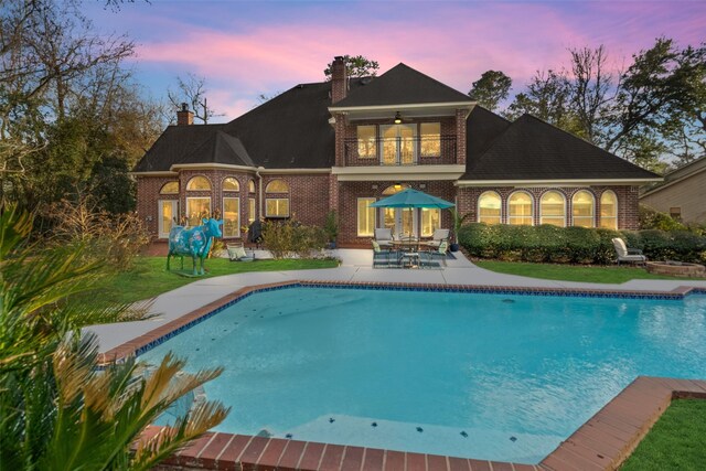 back house at dusk with ceiling fan, a balcony, and a patio area