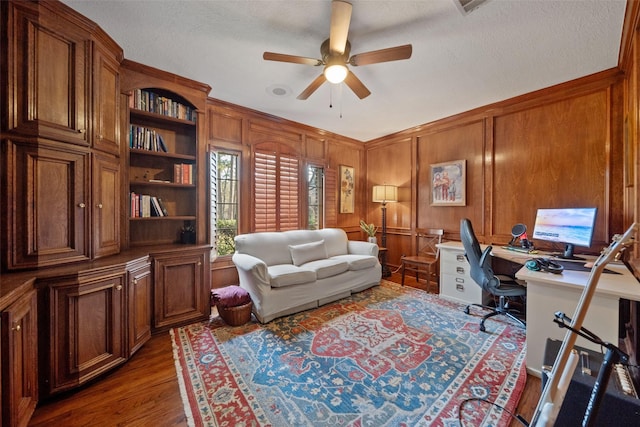 office featuring a textured ceiling, wooden walls, dark hardwood / wood-style floors, and ceiling fan