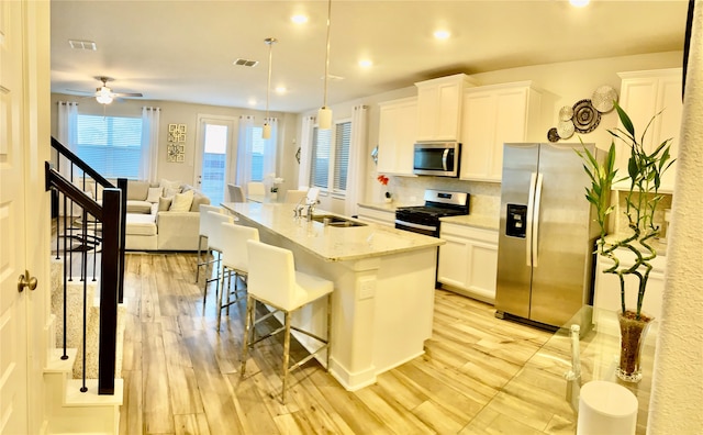 kitchen featuring a center island with sink, a kitchen breakfast bar, sink, hanging light fixtures, and appliances with stainless steel finishes