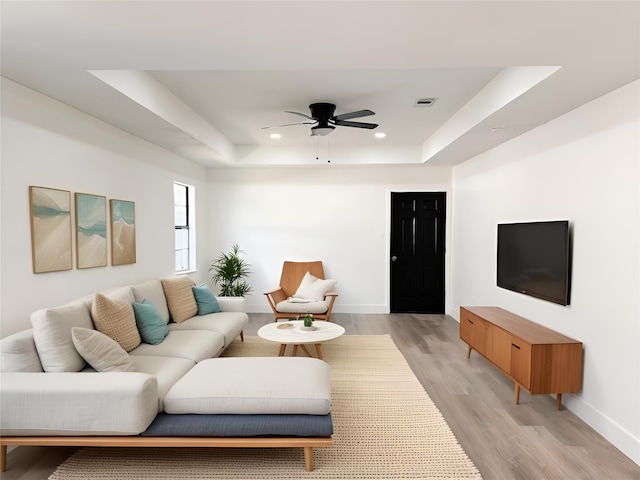 living room with light hardwood / wood-style floors, a raised ceiling, and ceiling fan