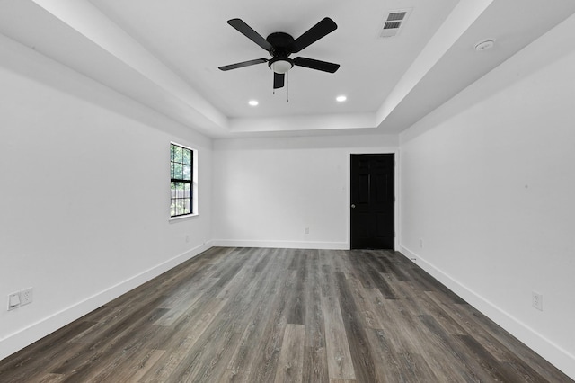 spare room featuring a raised ceiling, ceiling fan, and dark wood-type flooring