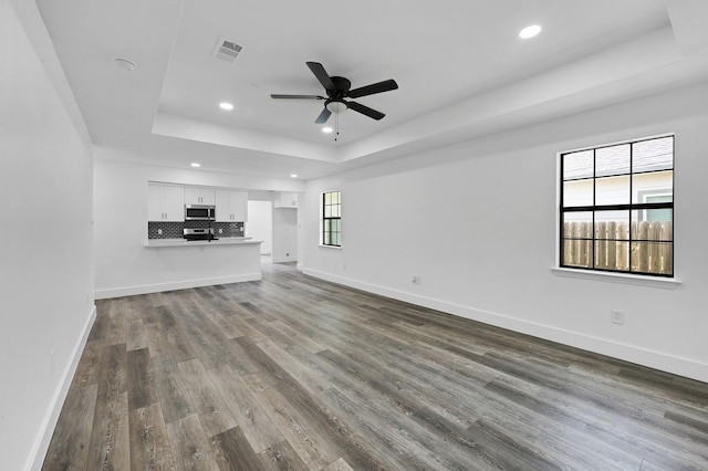 unfurnished living room with a tray ceiling, ceiling fan, and dark wood-type flooring